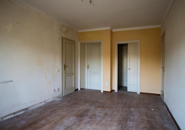 Soggiorno di una casa a Olbia prima della ristrutturazione con pavimento usurato e pareti da ripristinare